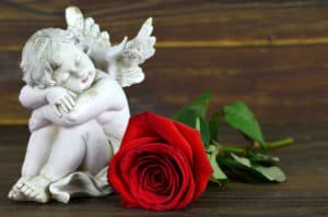 Little angel sleeping. Angel and red rose on wooden background