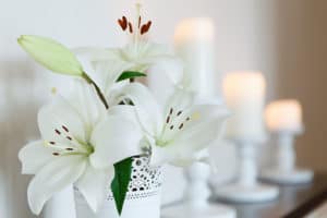 White lilies in a vase against a backdrop of candles. Flowers. Postcard