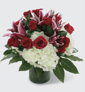 Make a daring, romantic statement with The Hearts Desire Bouquet for any loved one. The Hearts Desire Bouquet is a bespoke arrangement, beautifully designed featuring deep red roses, lush white hydrangea, and statement-making dark pink lilies set amongst tropical leaves and greenery and fashioned in a large clear cylinder vase. The perfect thoughtful gift for any romantic occasion.