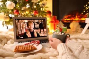 MYKOLAIV, UKRAINE - DECEMBER 23, 2020: Woman with sweet drink watching Home Alone movie on laptop at home, closeup. Cozy winter holidays atmosphere